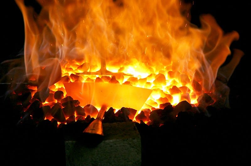 Glowing tool blade heating in the blacksmith's coal fire