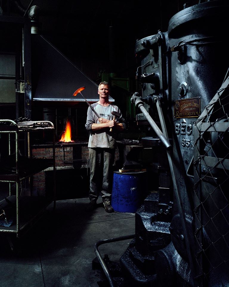 Sneeboer blacksmith holding a glowing hoe head and hammer beside the forge